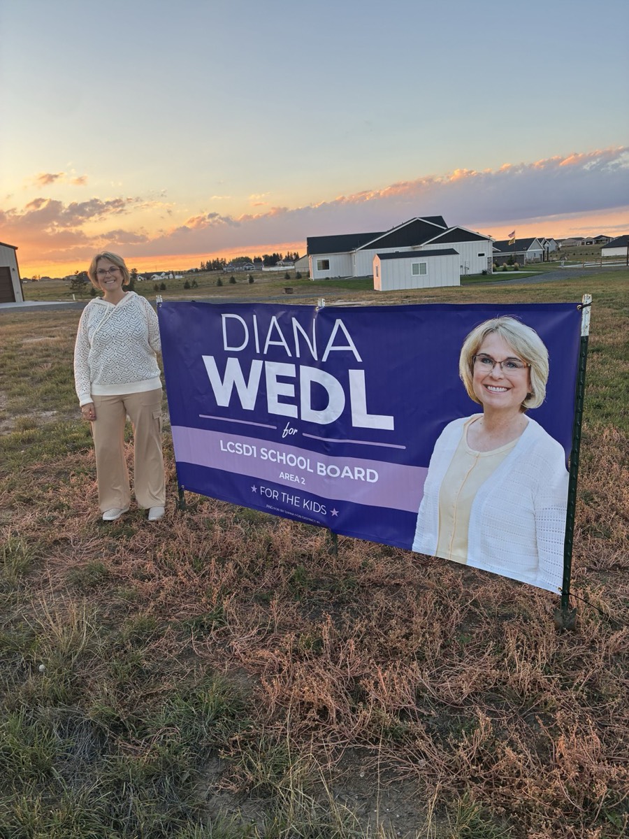 Diana standing beside her large campaign banner in a field at sunset.