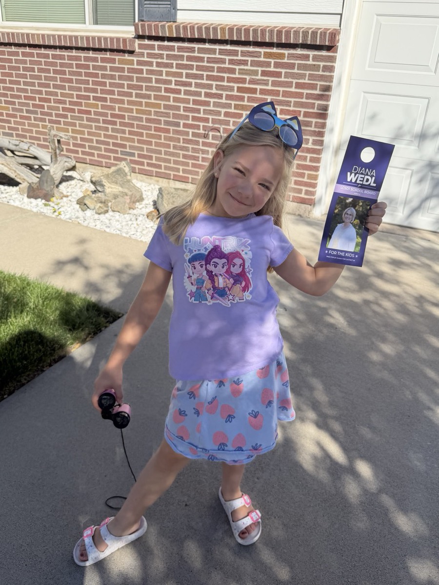 A young girl in a purple shirt smiling and holding up one of Diana's door hangers.