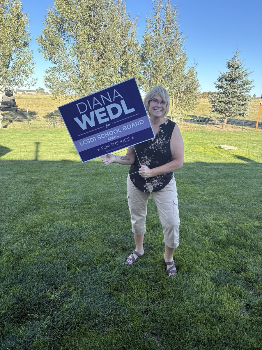 Diana standing on a lawn holding one of her purple yard signs.